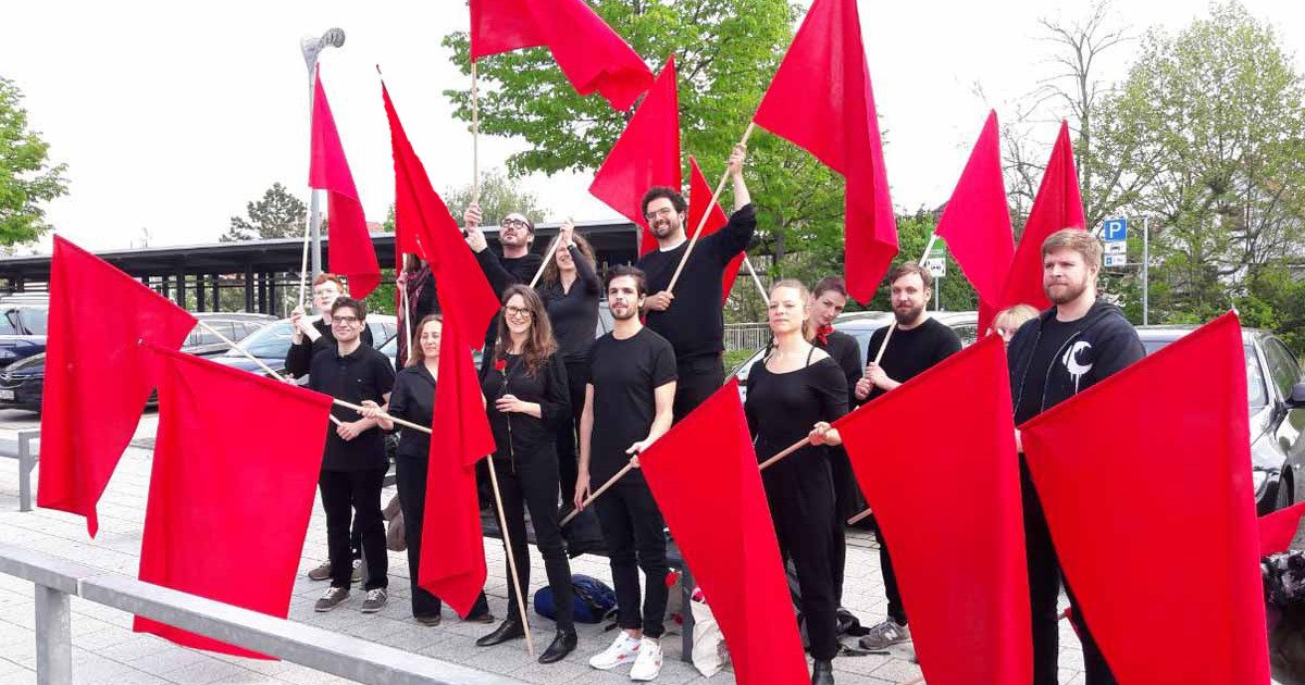 Foto vom Chor, der mit roten Fahnen am Straßenrand posiert.