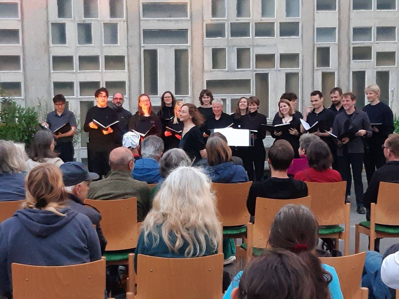 Der Chor steht vor der Philippus-Kirche Frankfurt-Riederwald. Im Vordergrund ist Publikum zu sehen.